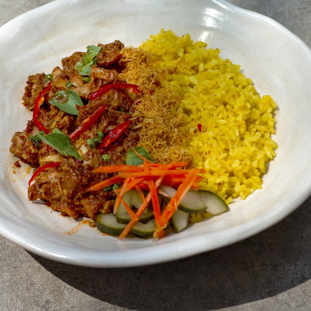 A plate of jack rendang, spicy Indonesian rendang with young jackfruit and tofu. Served with yellow rice, pickled carrots, cucumber, and serundeng (spiced grated coconut).